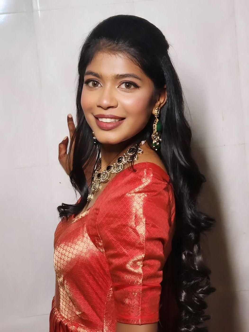 Woman in red saree with emerald necklace, soft glam makeup